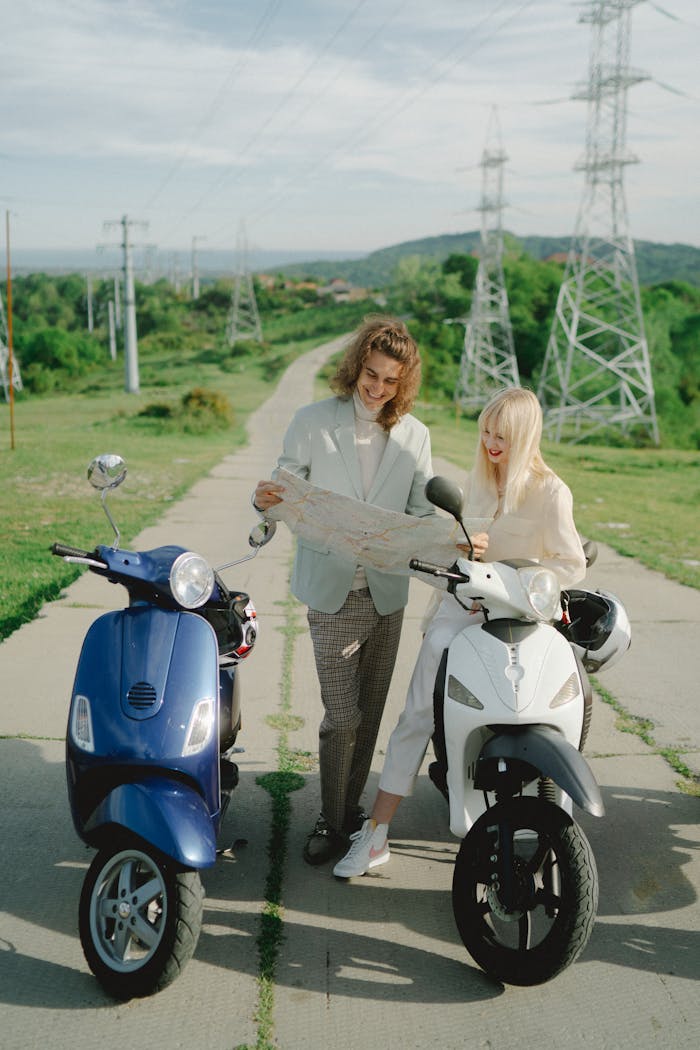 A smiling couple on scooters reading a map on a scenic rural road.